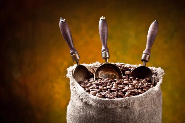 Sack of coffee beans and scoop. On a dark background. — Stock Photo, Image
