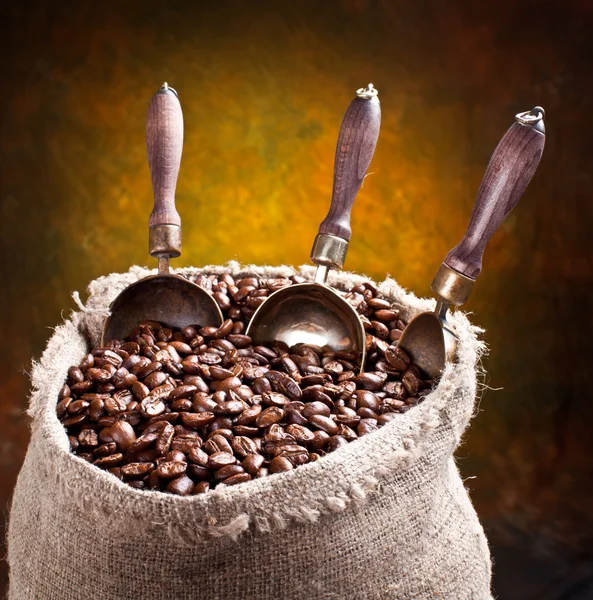 Un saco de granos de café y una cucharada. Sobre un fondo oscuro . —  Fotos de Stock