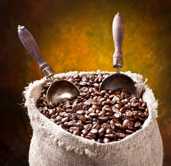 Un saco de granos de café y una cucharada. Sobre un fondo oscuro . —  Fotos de Stock