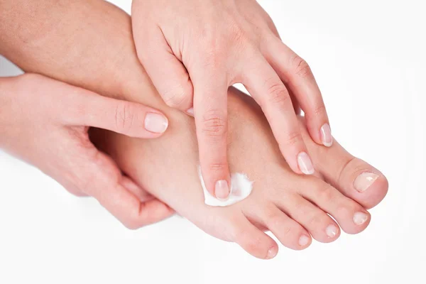 Giovane donna applica la crema sui suoi piedi. Su sfondo bianco . — Foto Stock