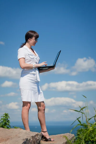 Business woman with laptop standing on a rock — Stock Photo, Image