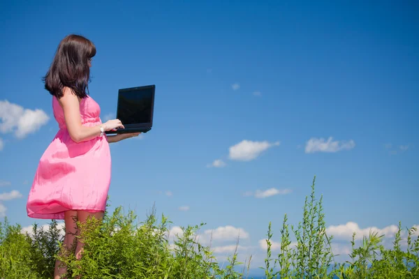 Belleza en rosa con un ordenador portátil en la naturaleza — Foto de Stock