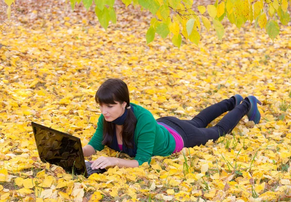 Ragazza con un computer portatile in un fogliame giallo autunno — Foto Stock