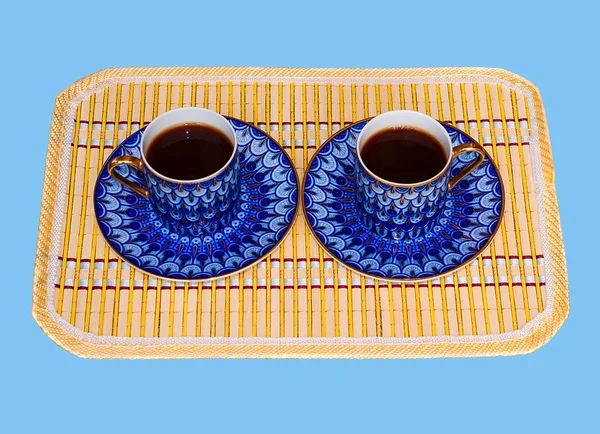 stock image Two elegant porcelain cups with coffee at a yellow bamboo mat