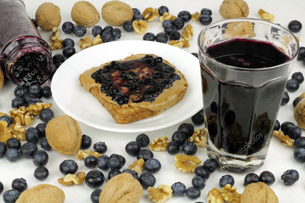 Blueberry preserves in jar on side and on almond butter on toast, blueberry juice, whole and shelled walnuts. Whole blueberries abstractly mixed with walnuts.