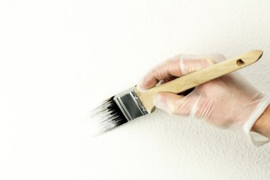 Home touch up painting off-white paint on wall with one and a half inch brush by vinyl gloved hand. clipart