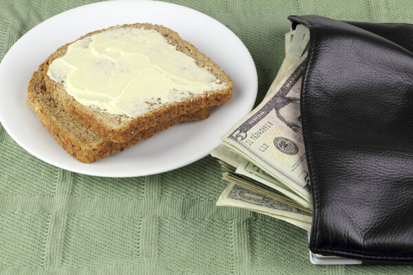 Два куска поджаренного цельного пшеничного хлеба на тарелке с американскими деньгами, выливающимися из кошелька
.