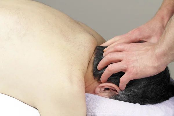 Mature man with graying black hair face down in a massage table receiving a scalp massage.
