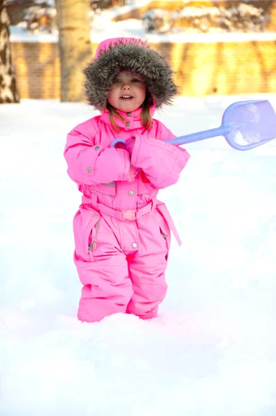 シャベルを使うと深い雪に防寒着立っている女の子 ストック画像