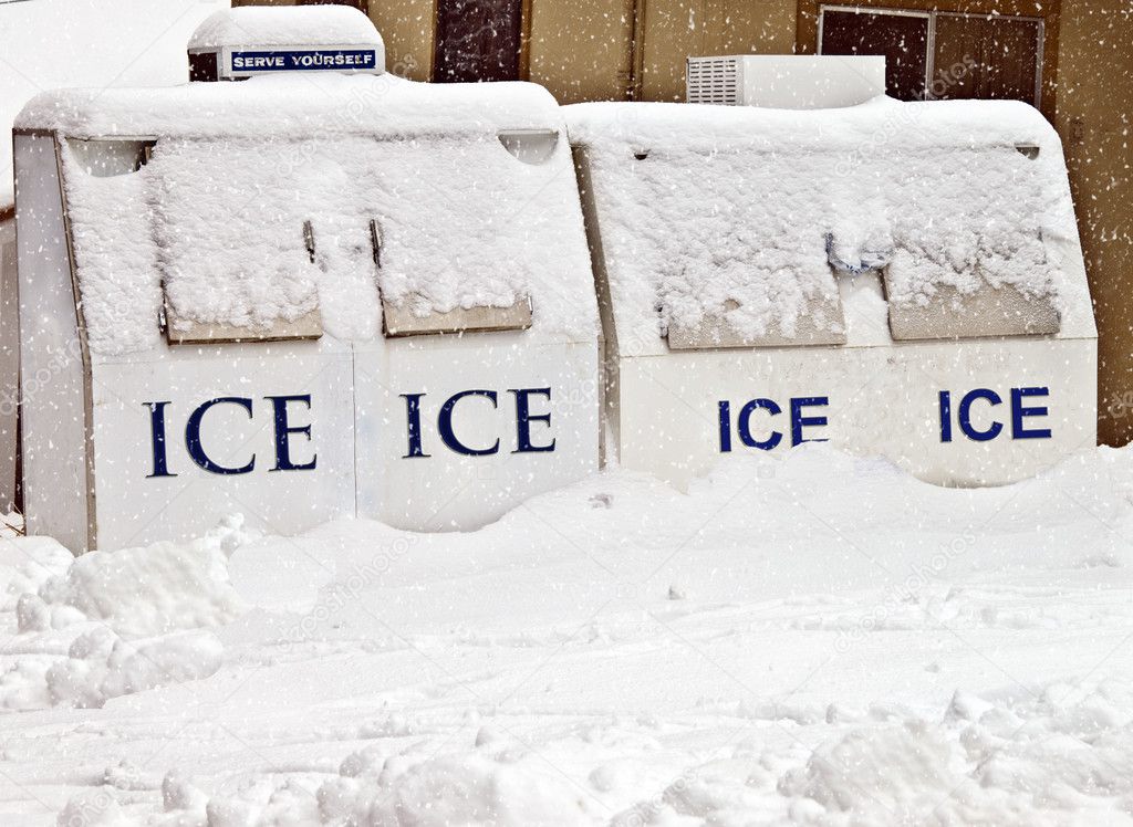 Ice machines in front of a store covered in snow during a storm.