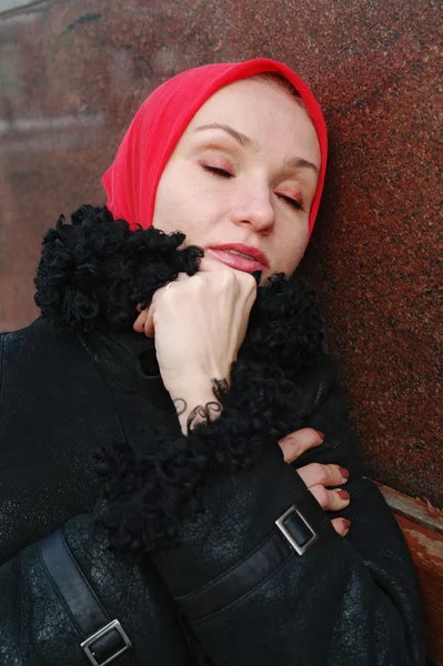Smutná dívka v červeným šátkem a černý kabát sedí na lavičce — Stock fotografie