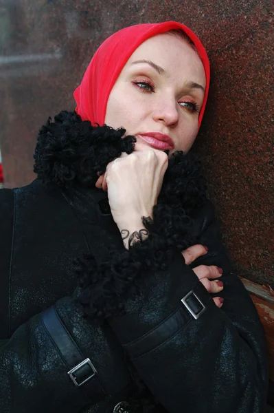 Грустная девушка в красном шарфе и черном пальто сидит на скамейке — стоковое фото