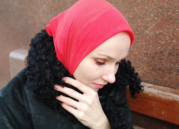 Het trieste meisje in een rode sjaal en een zwarte jas zit op een bankje — Stockfoto
