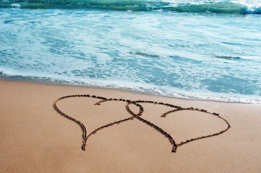Two hearts drawn on the sand of a beach clipart