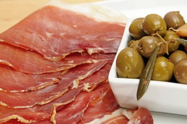 A pile of spanish serrano ham and a bowl with marinated olives clipart