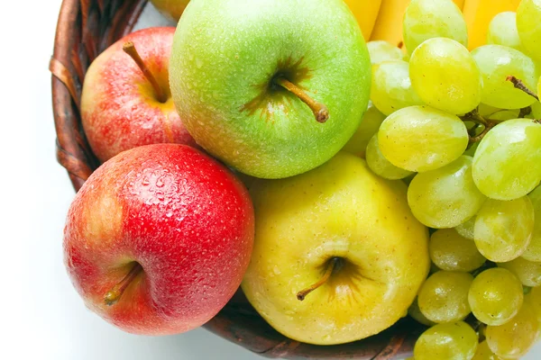四个不同颜色的苹果放在与一些葡萄和香蕉在白色孤立的柳条篮 — 图库照片