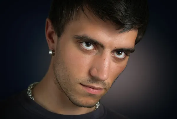 stock image Portrait of beautiful and attractive young man with penetrating eyes and a silver earring in closeup on dark background