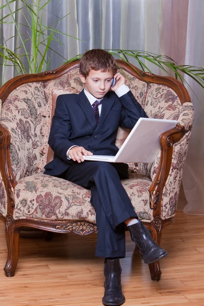 Jovem menino confiante vestido em terno de negócios sentado com comput — Fotografia de Stock