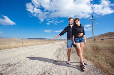 Fashion couple try to stop the car on old road clipart