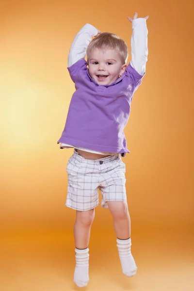 Salto feliz bonito menino em violeta t-shirt — Fotografia de Stock