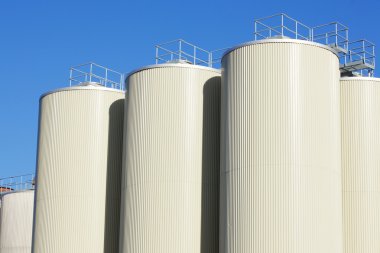 Refinery oil storage tanks and blue sky in background clipart