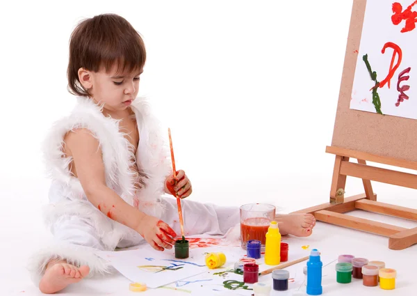 Симпатичный сидящий ребенок в белой живописи с кистью возле кисти — стоковое фото