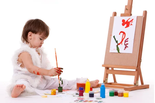 Söt sitter barnet i vit målning med pensel nära staffli — Stockfoto