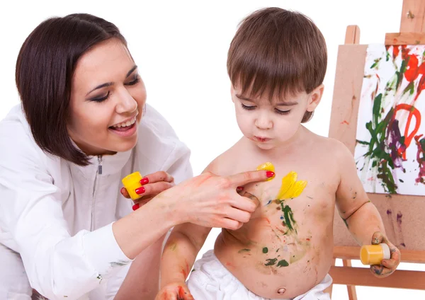 Bromeando madre feliz pintando el cuerpo de su hijo cerca del caballete —  Fotos de Stock