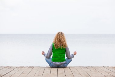 yoga kadın geri okyanus yakın ahşap köprü üzerinde oturuyordu