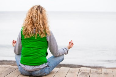 yoga kadın okyanus yakın ahşap köprü üzerinde oturuyordu