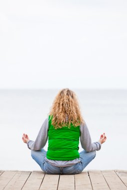 yoga kadın geri okyanus yakın ahşap köprü üzerinde oturuyordu