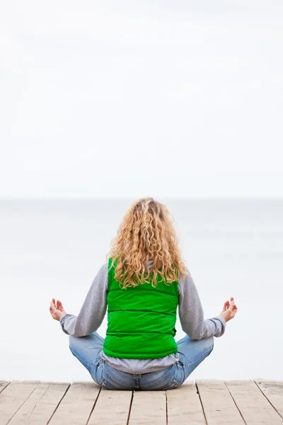 stock image Yoga woman sitting back on wooden bridge near the ocean