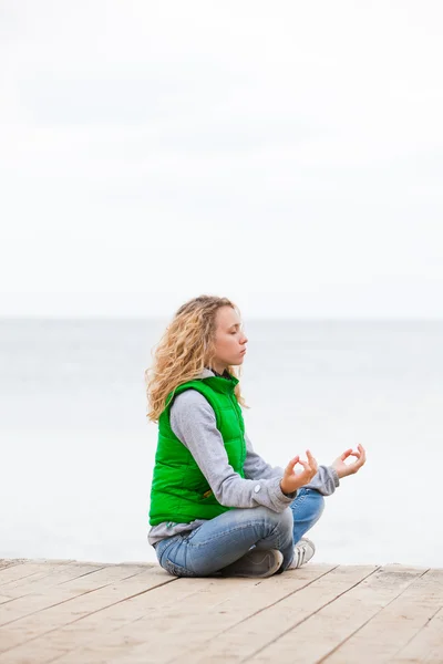 Yoga kvinnan sitter på träbro nära havet — Stockfoto