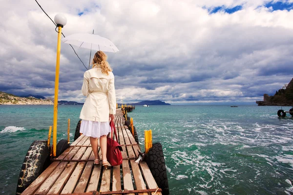 Mujer con paraguas y bolsa a manos caminando sobre un pie de mar de madera — Foto de Stock