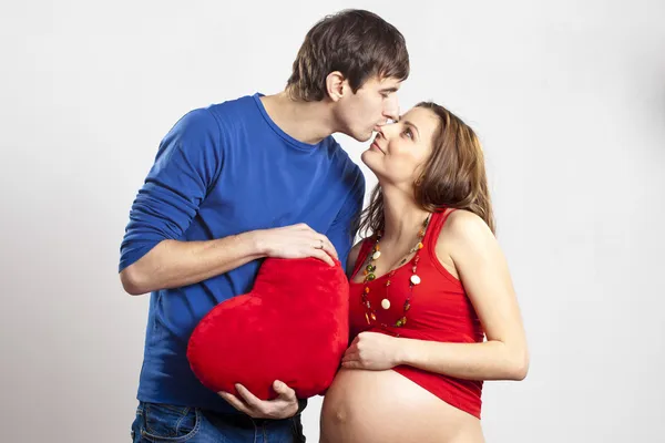 赤いハートを保持している彼の妊娠した妻の鼻にキス男 — ストック写真
