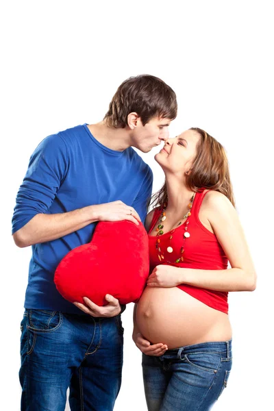 Gelukkige grapje paar omarmen zwangere buik en rood hart — Stockfoto