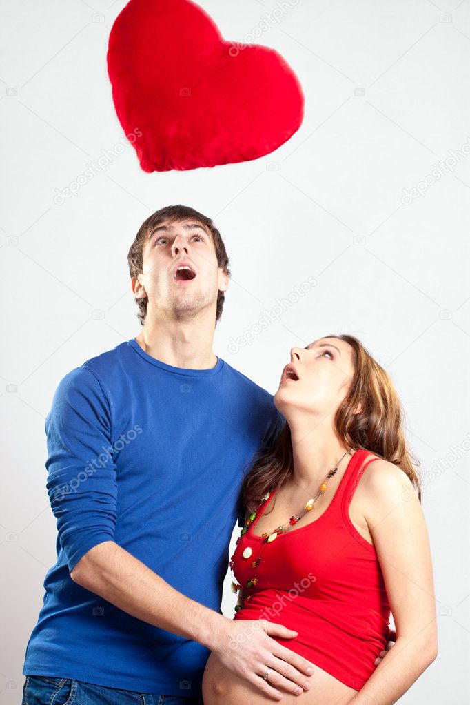 Man and pregnant woman looking up at red heart