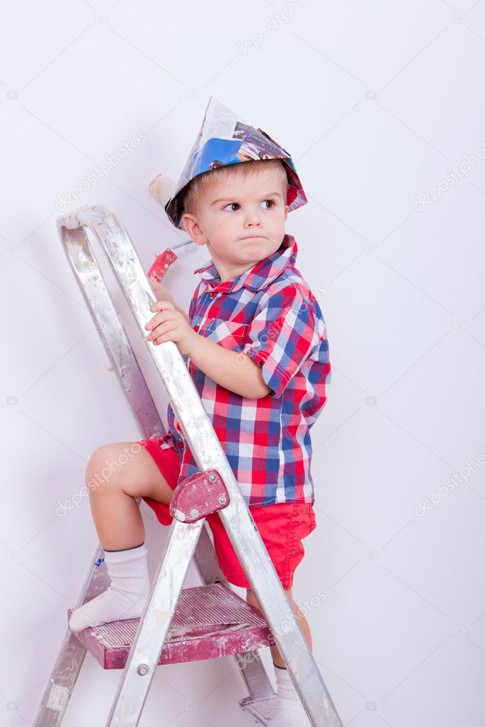 Little angry boy on ladder painting wall with roller