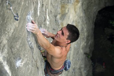 Male rock climber clings to an overhang in rock clipart