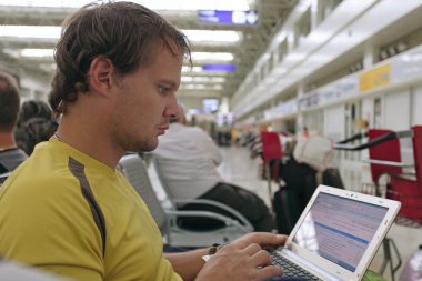 Male traveler working on his laptop computer in the airport clipart