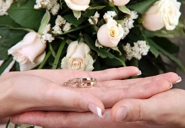 Обручальные кольца в руке на фоне букета роз — стоковое фото