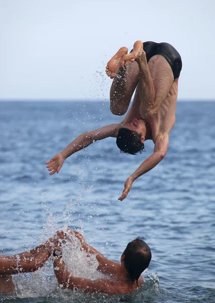 Amigos varones jugando en el mar, uno realizando salto mortal — Foto de Stock