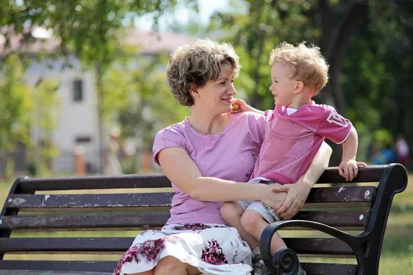 Счастливые мать и сын сидят на скамейке в городском парке — стоковое фото
