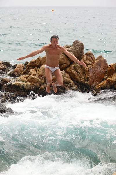 젊은 남자가 바위의 더미에서 물으로 점프 — 스톡 사진