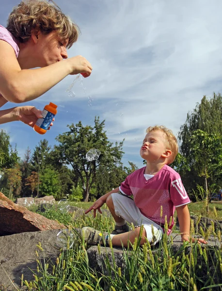 Mor och son blåser såpbubblor i en park — Stockfoto