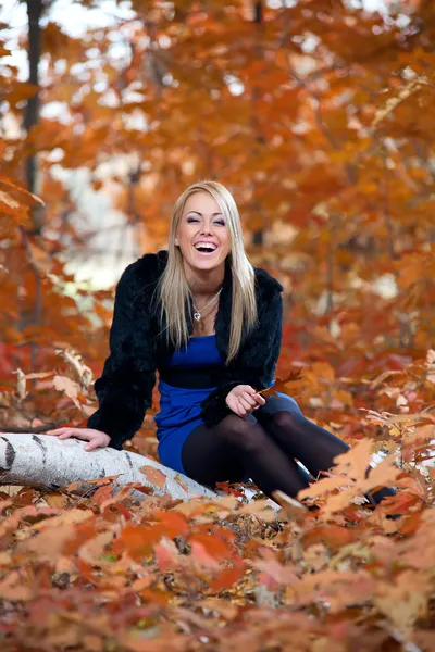 Yapraklar sonbaharda karşı ağaç üzerinde oturan genç kadın — Stok fotoğraf