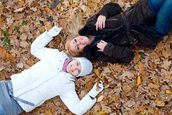 Dos amigas tumbadas en hojas de otoño — Foto de Stock