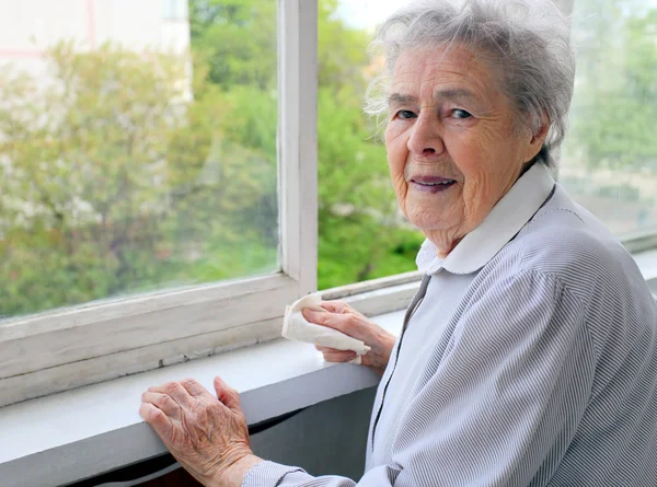 Portrait of senior woman standing at the window at her home — Stock Photo, Image