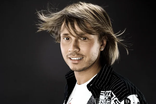 Retrato de jovem bonito homem com cabelo balançando no vento em fundo preto no estúdio — Fotografia de Stock