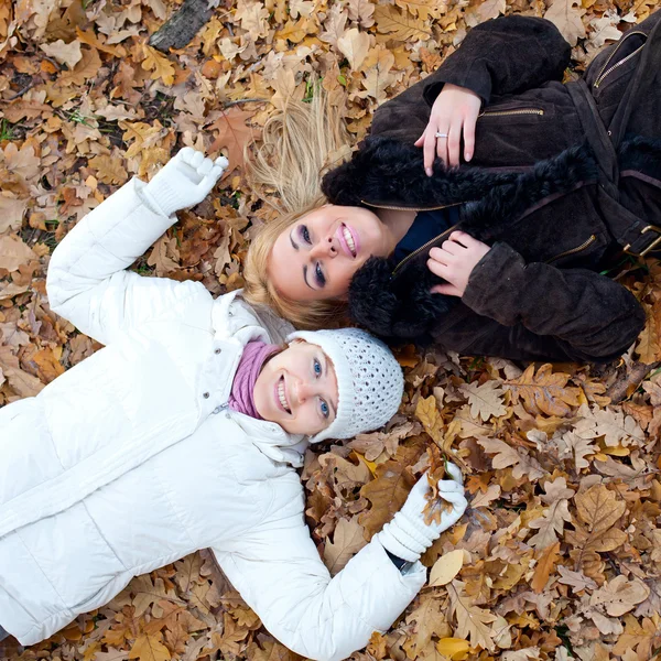 Two female friends lying down in autumn leaves — Stock Photo, Image